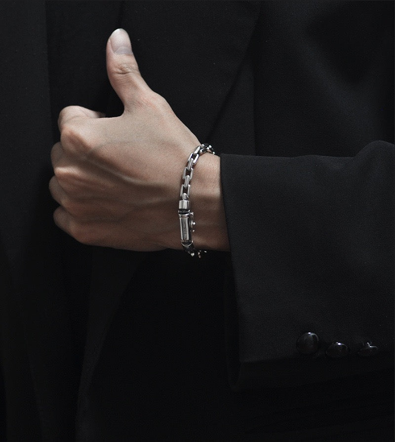 Hand wearing a silver bracelet giving a thumbs-up gesture against a dark background