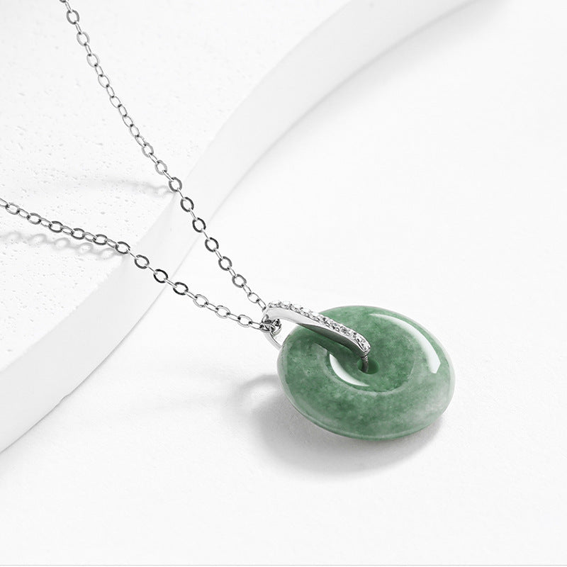 Side profile view of a polished natural green jadeite doughnut pendant showing its thickness and platinum-plated silver inlay.