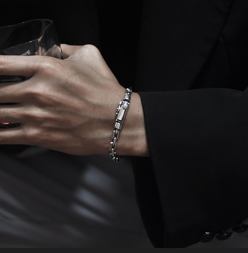 Hand wearing a silver bracelet holding a glass against a dark background