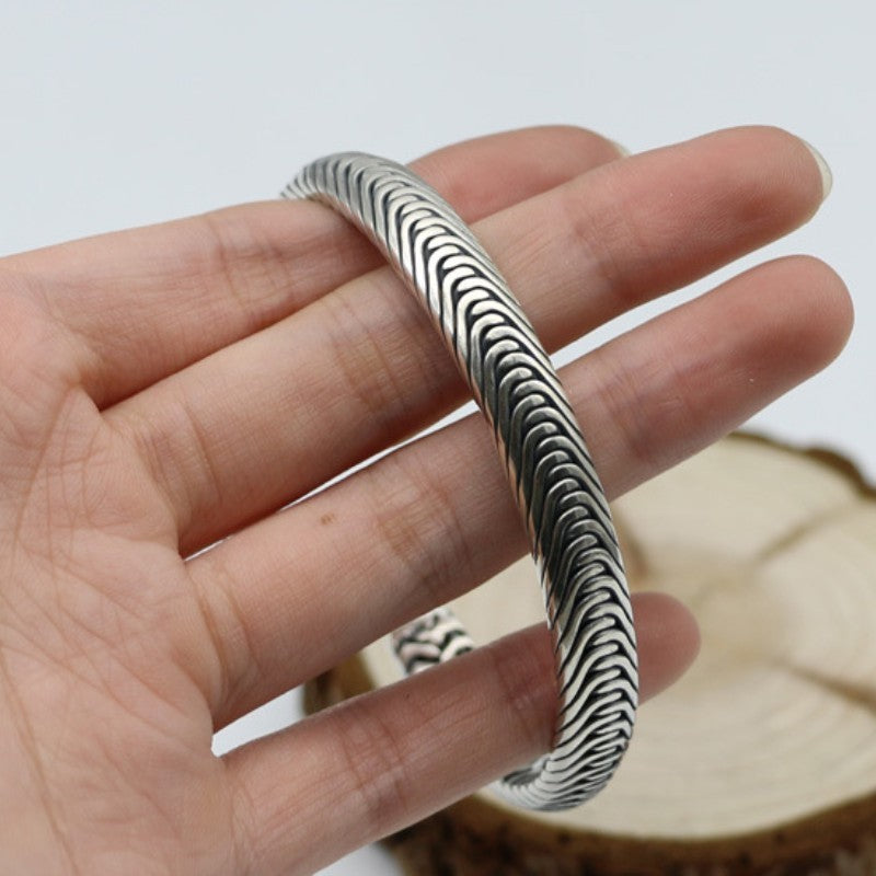 A close-up macro shot of a hand holding the Nordic Frost Braided Silver Cuff to show scale. The continuous, fluid ridges of the tightly packed silver chevron links are sharply in focus, emphasizing the thick gauge and elite artisan texture of the piece.