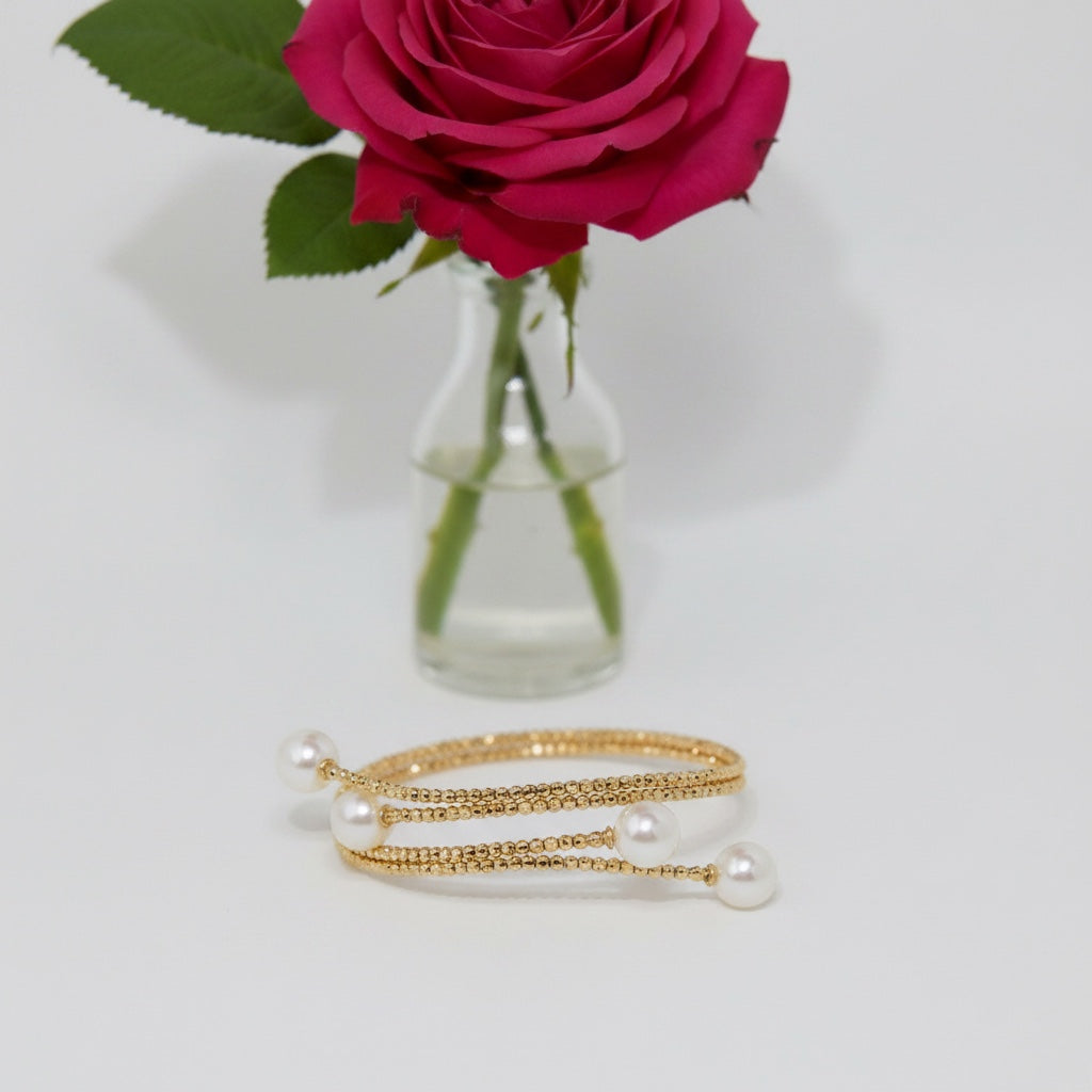 BoxUnboxed 18K yellow gold multi-coil spiral bangle with Akoya pearls. Features diamond-faceted beads and a flexible cuff design.