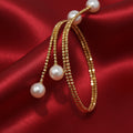 BoxUnboxed 18K yellow gold spiral bangle with diamond-cut beads and three Akoya pearls. Flexible cuff design.