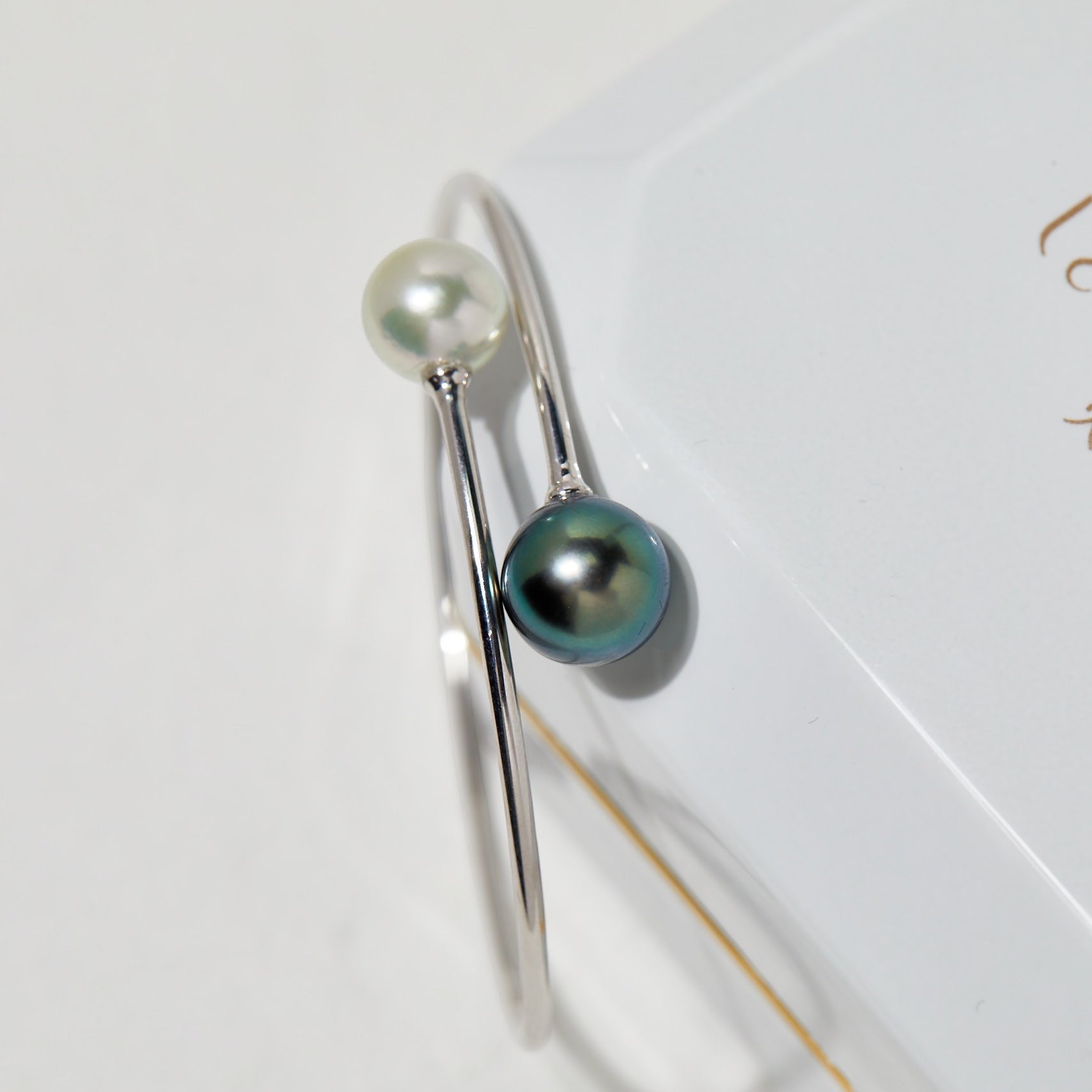BoxUnboxed 18K white gold bypass bangle with a white Akoya pearl and a dark Tahitian pearl.