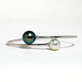 BoxUnboxed 18K white gold bypass bangle with a dark peacock Tahitian pearl and a white Akoya pearl.